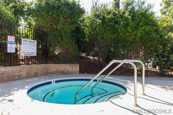Outdoor spa area with a small round pool and metal handrails, surrounded by a fence and greenery.