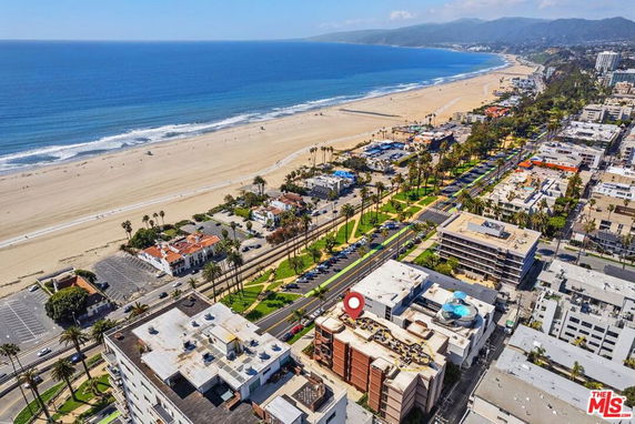 Aerial view of a coastal city with buildings, palm trees, roads, and a wide sandy beach along the ocean.