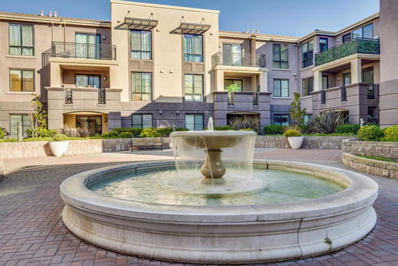 Front view of a multi-story apartment building with balconies and a central courtyard fountain.