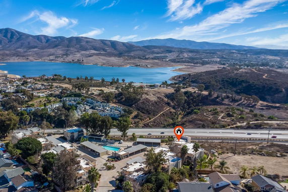 Aerial view of residential area near a highway and a lake, surrounded by hills.