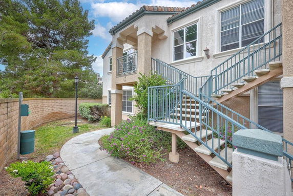 Front view of a two-story house with external stairs and a small garden area.