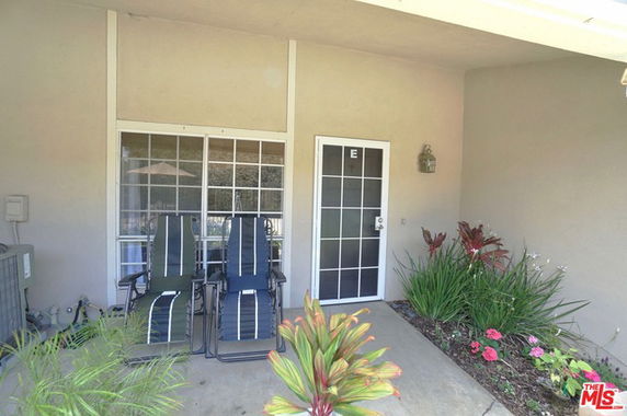 Front view of a building with a door and a window, accompanied by two lounge chairs and potted plants.