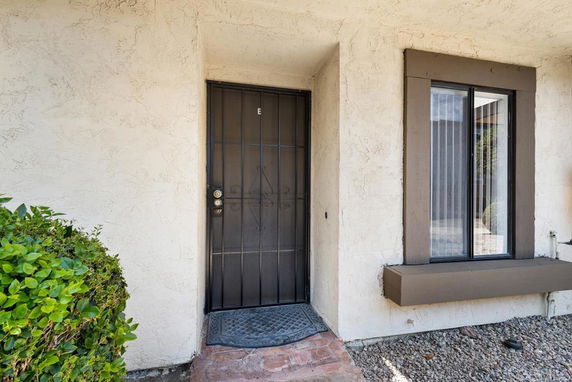 Front entrance of a building with a black metal door and adjacent window with shutters.