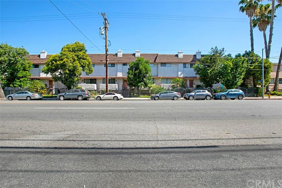 Front view of a row of townhouses with multiple chimneys and trees in front.