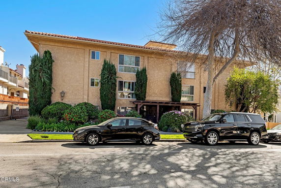 Front view of a multi-story residential building with tall windows and shrubbery.
