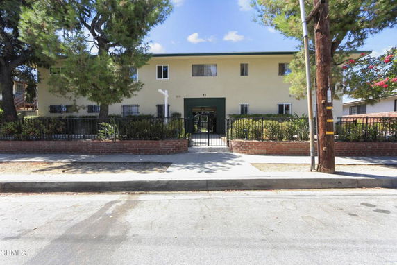 Front view of a two-story residential building with a brick fence and gated entrance.