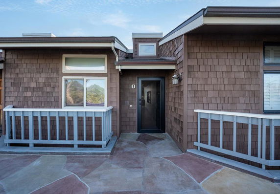 Front view of a house with brown shingle siding and a glass door.