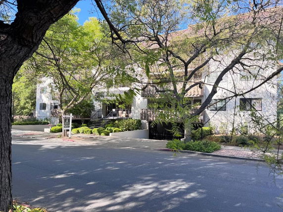 Front view of a multi-story residential building with a balcony and trees surrounding it.
