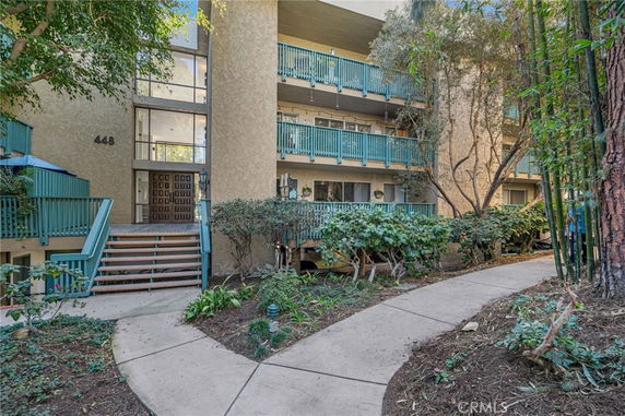 Front view of an apartment building with teal balconies and a pathway leading to the entrance.