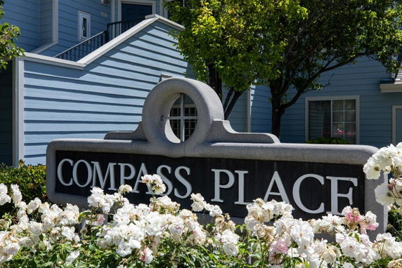 Front view of a blue house with a sign reading 'Compass Place' in the foreground.