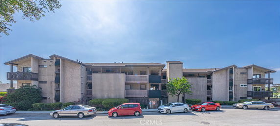 Front view of a multi-story residential building with balconies and parking space in front.