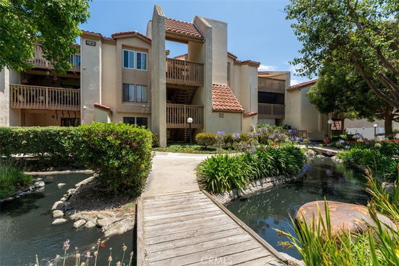 Front view of a multi-story building with balconies and a walkway over a pond.