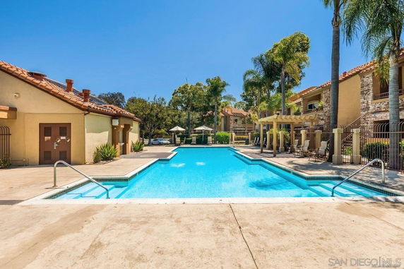 Outdoor swimming pool area with surrounding buildings and palm trees.