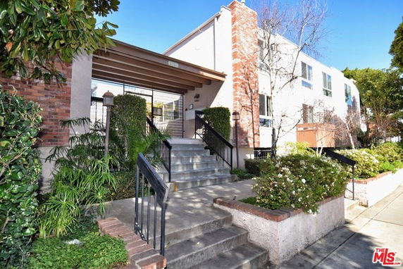 Front view of a two-story building with brick and stucco facade, featuring stairs and a covered entrance.