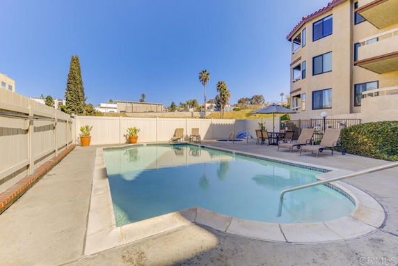 Outdoor swimming pool area with lounge chairs and umbrellas beside a multi-story building.