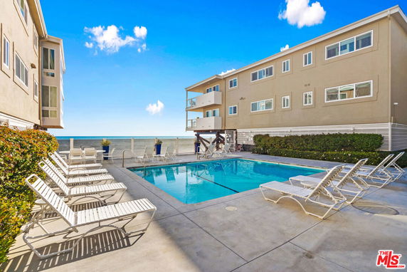 Outdoor swimming pool area next to a multi-story building by the ocean.