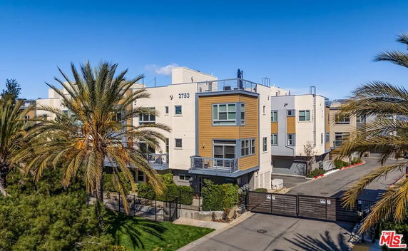 Front view of a multi-story apartment building with balconies and a gated entrance.