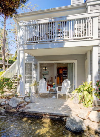 Front view of a two-story house with a balcony and patio by the water.