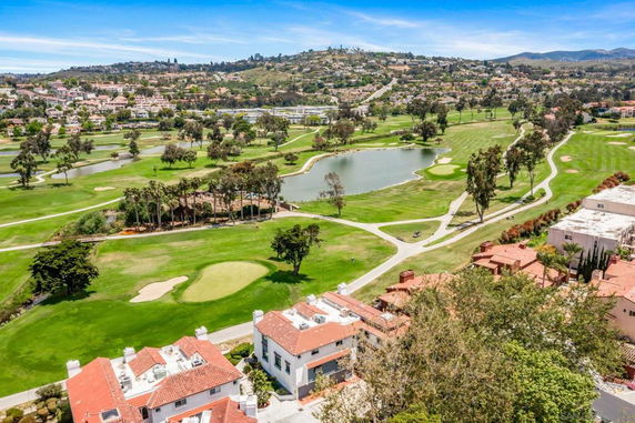 Aerial view of a landscape with golf course, ponds, and surrounding hills and buildings.
