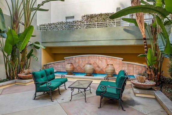 Outdoor seating area with green cushions and decorative pots on a tiled wall.