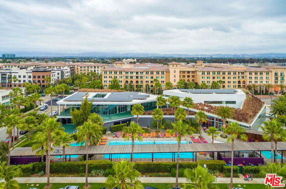 Wide view of a modern building complex with a swimming pool area and surrounding residential structures.