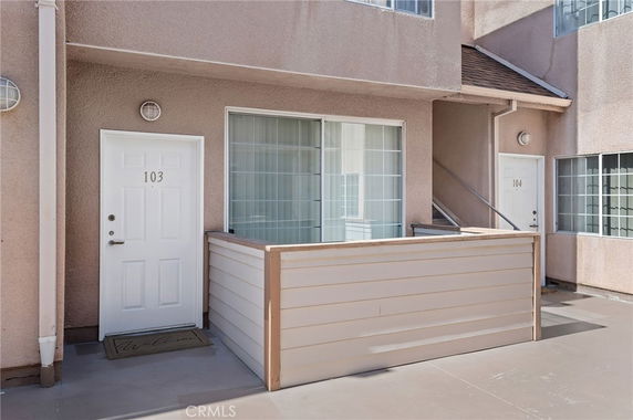Front view of an apartment or condo unit with an entrance door numbered 103 and a small external patio area.