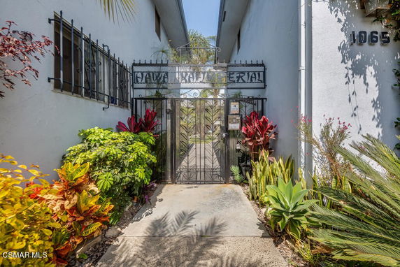 Exterior view of a building entrance with a decorative metal gate and surrounding plants.