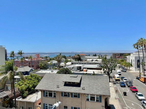 Panoramic view of a coastal cityscape with buildings, roads, and trees, overlooking a body of water.