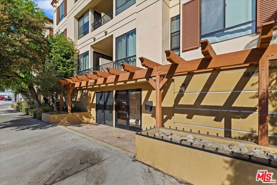 Front view of a multi-story building with balconies and a wooden pergola at the entrance.