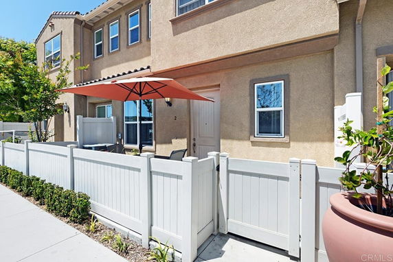 Front view of a two-story house with a fenced patio and umbrella.