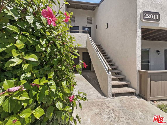 View of a two-story building with exterior stairs and a small patio area.