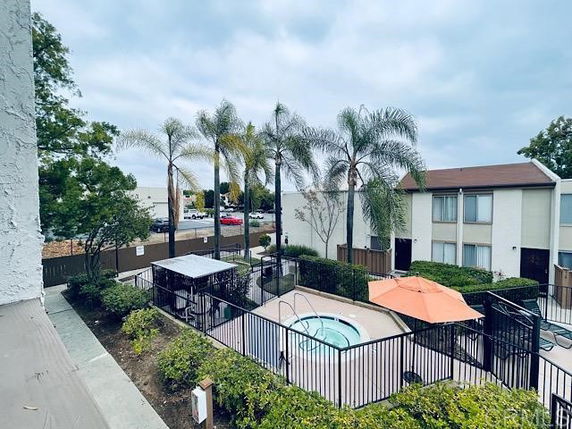Outdoor swimming pool area surrounded by a fence and landscaping, with apartment buildings in the background.