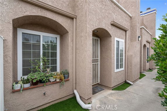 Front view of a stucco-finished townhouse with arched windows and plants on the ledge.