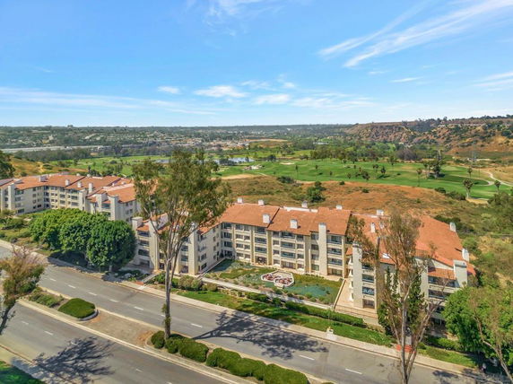 Aerial view of apartment buildings with red roofs overlooking a golf course and surrounding landscape.