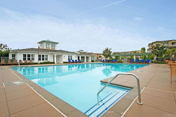 Outdoor swimming pool area with lounge chairs and a clubhouse in the background.
