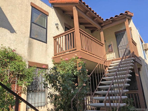 Front view of a two-story building with an external staircase and wooden balcony.