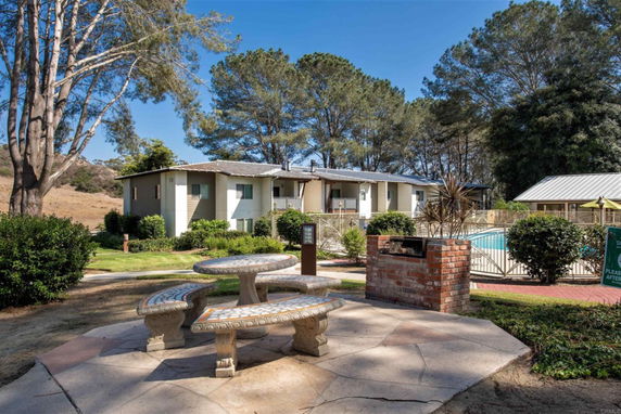 Outdoor view showing a two-story building with a fenced swimming pool area and trees in the background.