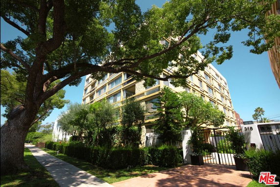 Front view of a multi-story residential building with trees and greenery.