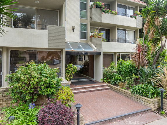 Front view of a multi-story residential building with balconies and a landscaped entrance.