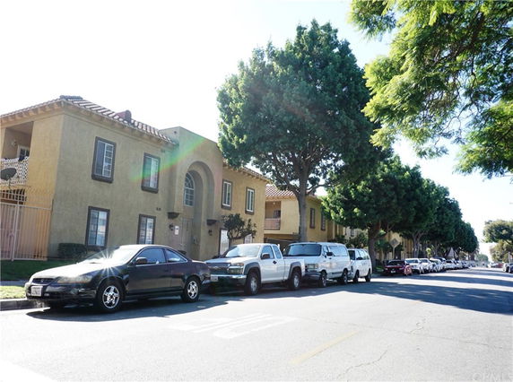 Front view of a beige two-story apartment building with multiple windows and parked cars.