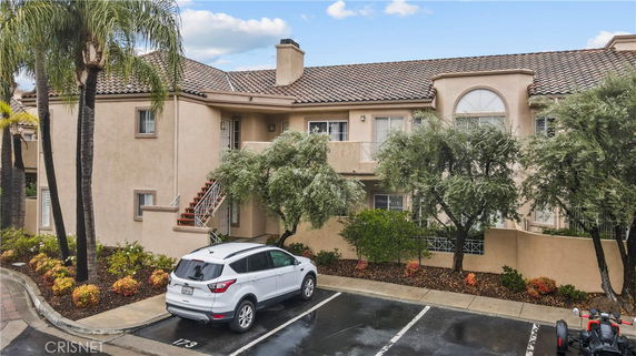 Front view of a two-story residential building with a tiled roof and parking area.