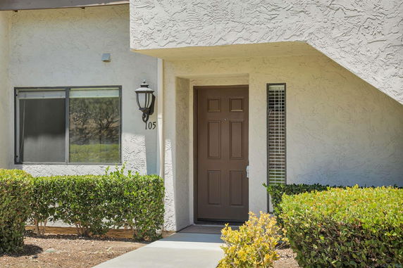 Front view of a building with a door and window, surrounded by shrubs.