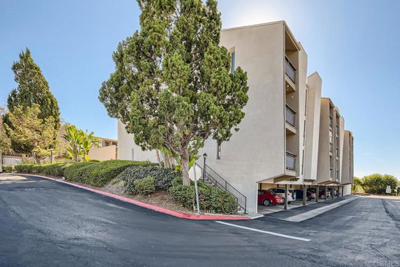 Front view of a multi-story building with covered parking spaces underneath.