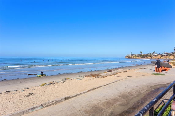 Wide-angle view of a beach with surfers and cliffs in the background.