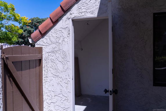 Front view of a stucco house with a red-tile roof and open wooden gate.