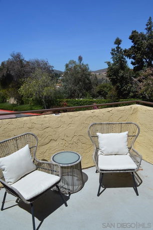 Rooftop area with two chairs and a small table, surrounded by trees and hills in the background.
