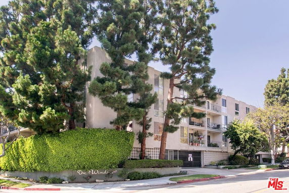 Front view of a multi-story building with balconies and surrounding trees.