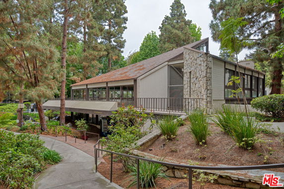 Front view of a single-story building with large windows and a sloped roof, surrounded by trees.