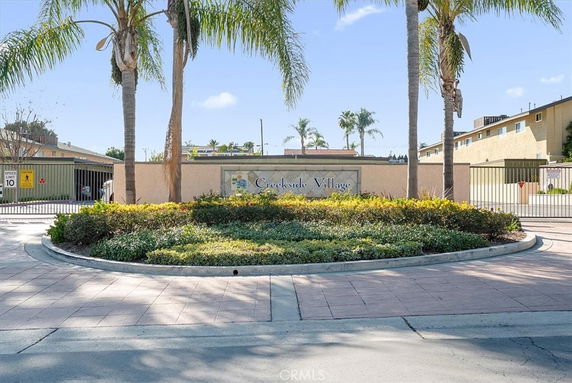 Front view of a gated residential complex entrance with palm trees and signage.