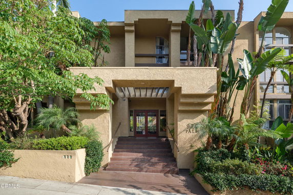 Front view of a multi-story building with an entrance and stairs surrounded by greenery.
